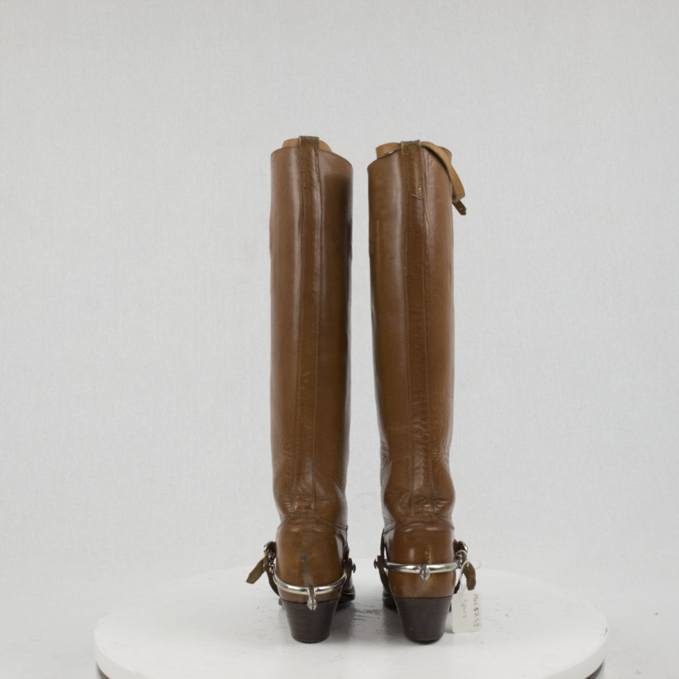Image of a pair of calf high, brown leather riding boot, coupled with a set of small silver spurs.