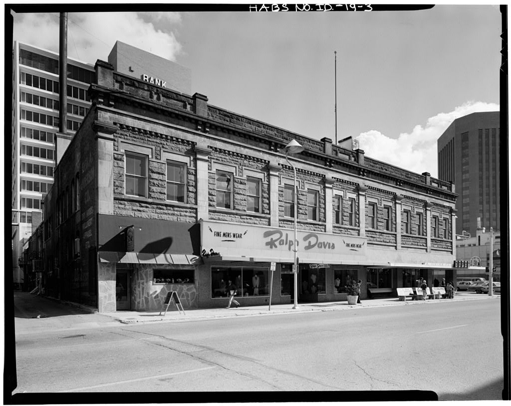 Black and white photo of a large sandstone two-story building showing the storefront space now taken up by Ralph Davis Menswear