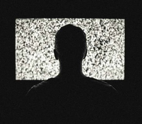 dark silhouette of a man's head starting at a static tv screen